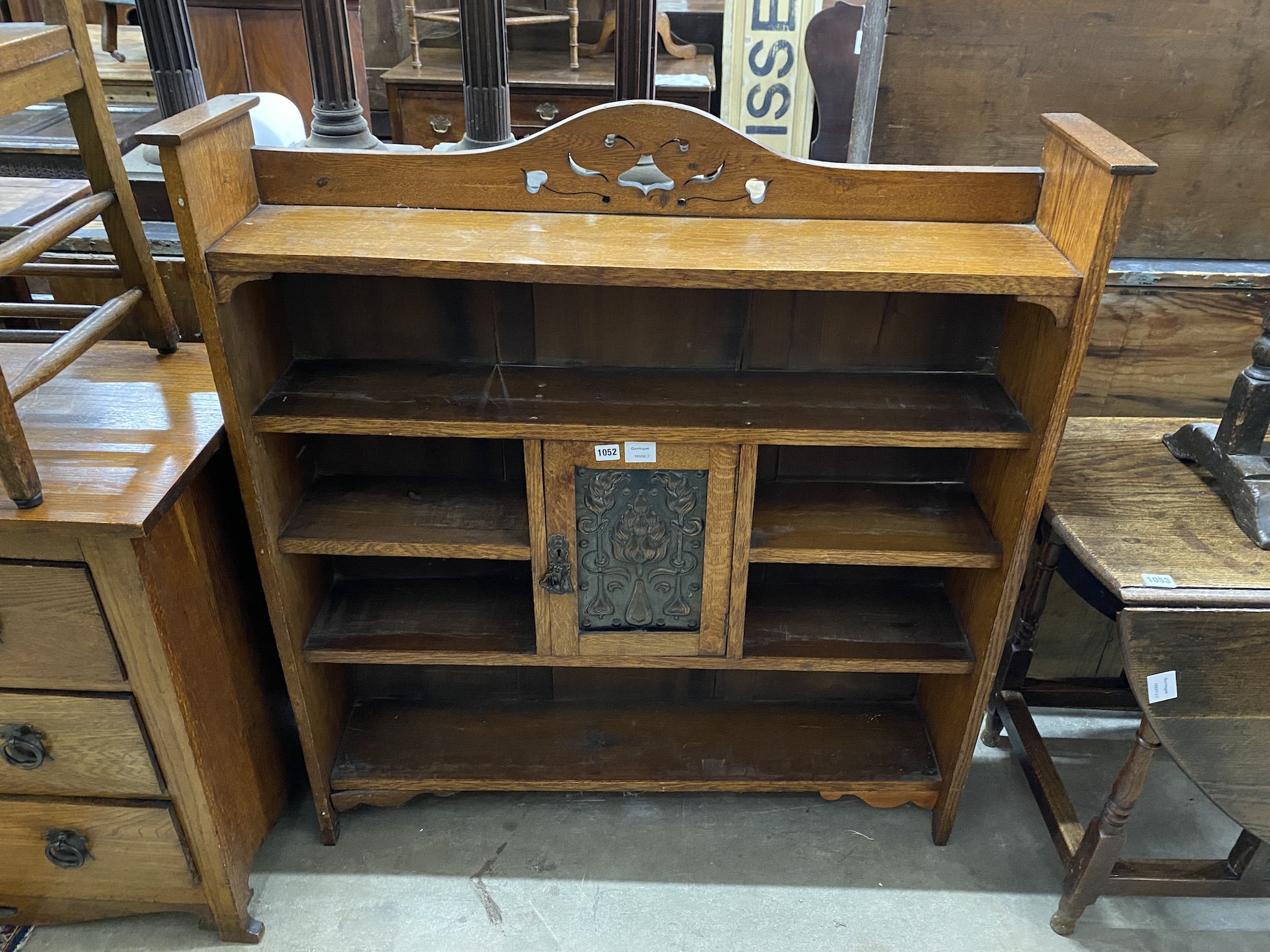 An Art Nouveau oak open bookcase, fitted with a central cupboard, the door inset with a hammered copper panel, width 106cm, depth 23cm, height 113cm